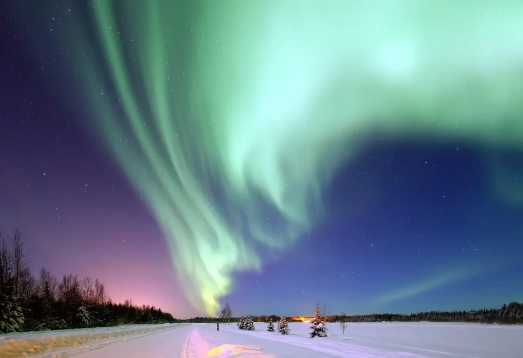 Northern Lights over snowy landscape with dancing green aurora bands above mountains