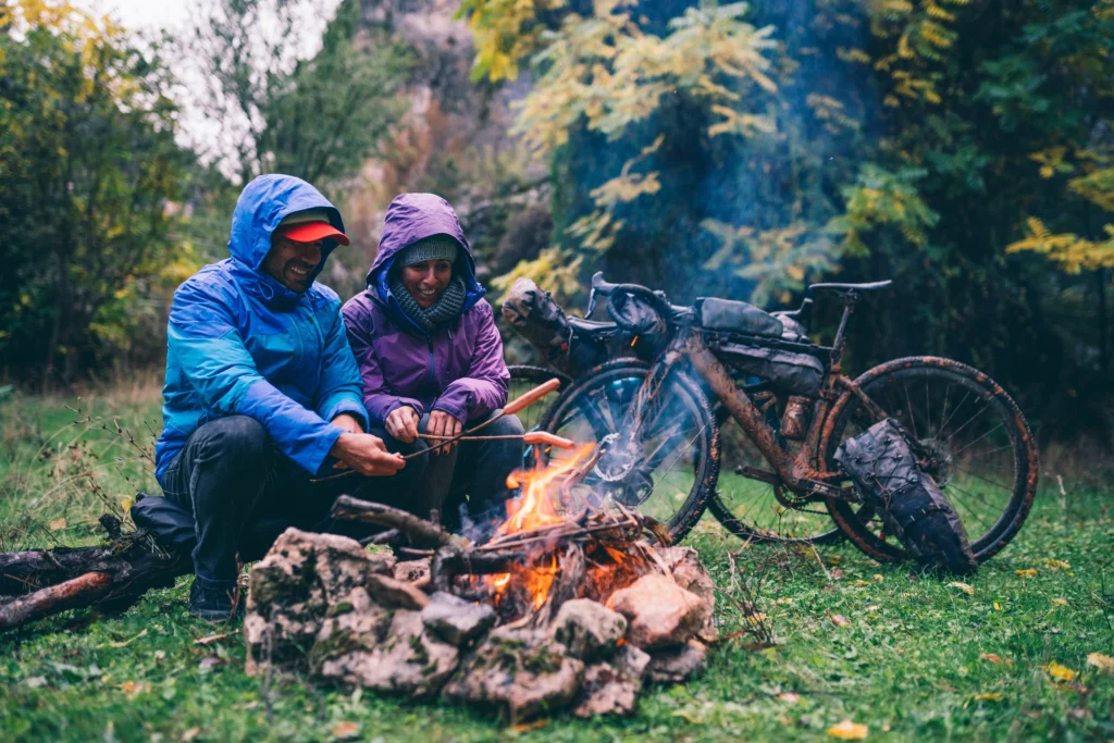Adventure travelers cooking outdoors during a rain shower, laughing and having fun